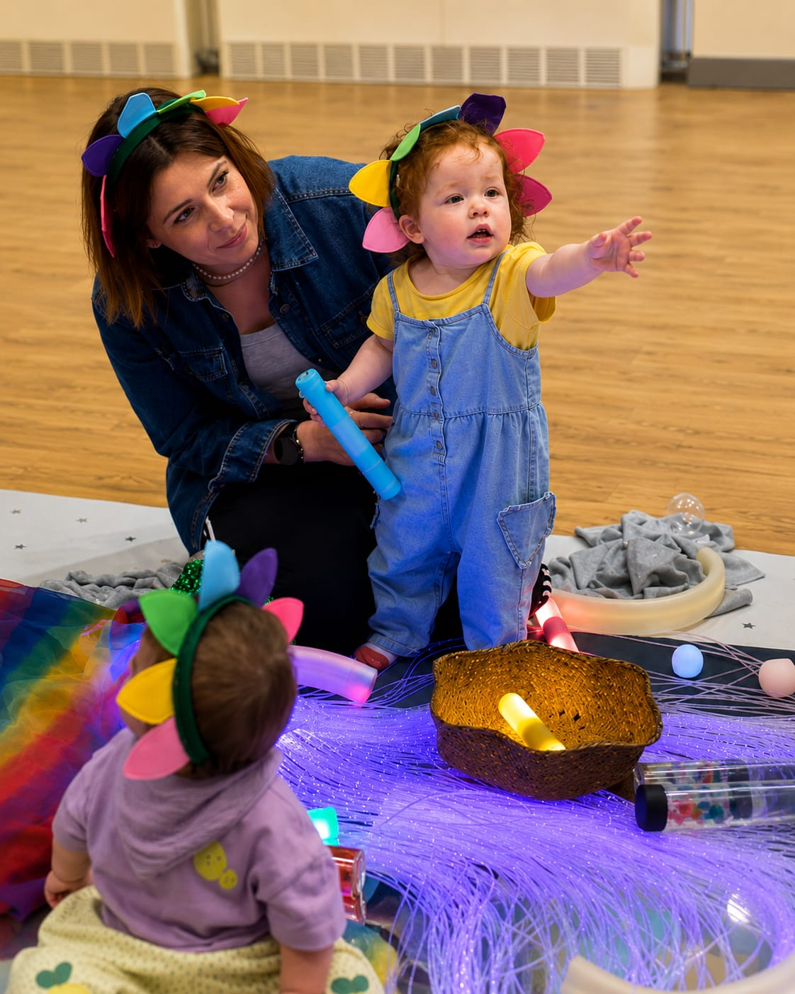 Mum and toddlers in colourful flower headbands exploring sensory play at a Baby Babble NI class